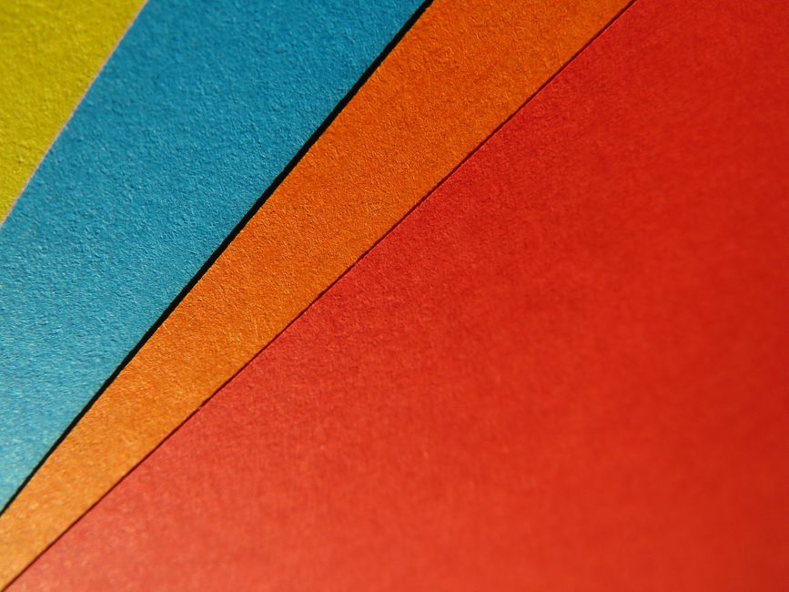 A colorful layout of printed kindergarten language arts worksheets on a wooden table with crayons and safety scissors.