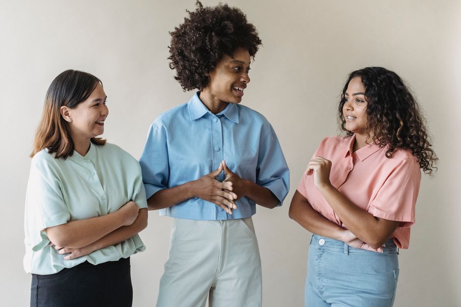 A diverse group of people smiling and communicating using American Sign Language in a bright classroom setting.