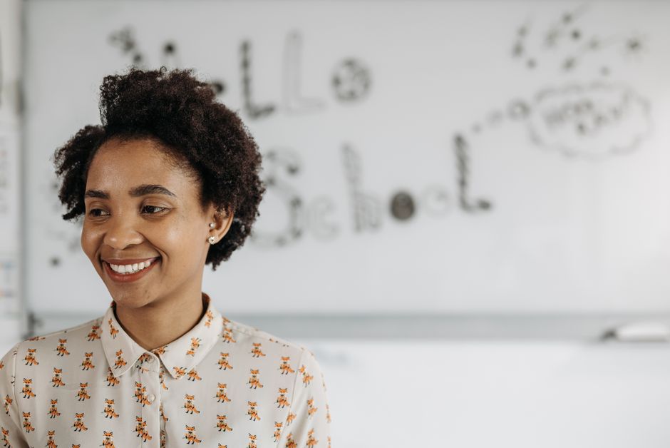 A smiling instructor demonstrating a basic ASL sign in a bright, welcoming classroom setting.