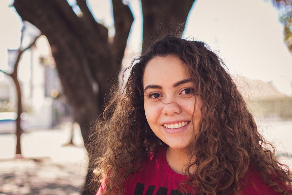 A young woman smiling while practicing American Sign Language handshapes in a bright, welcoming room.